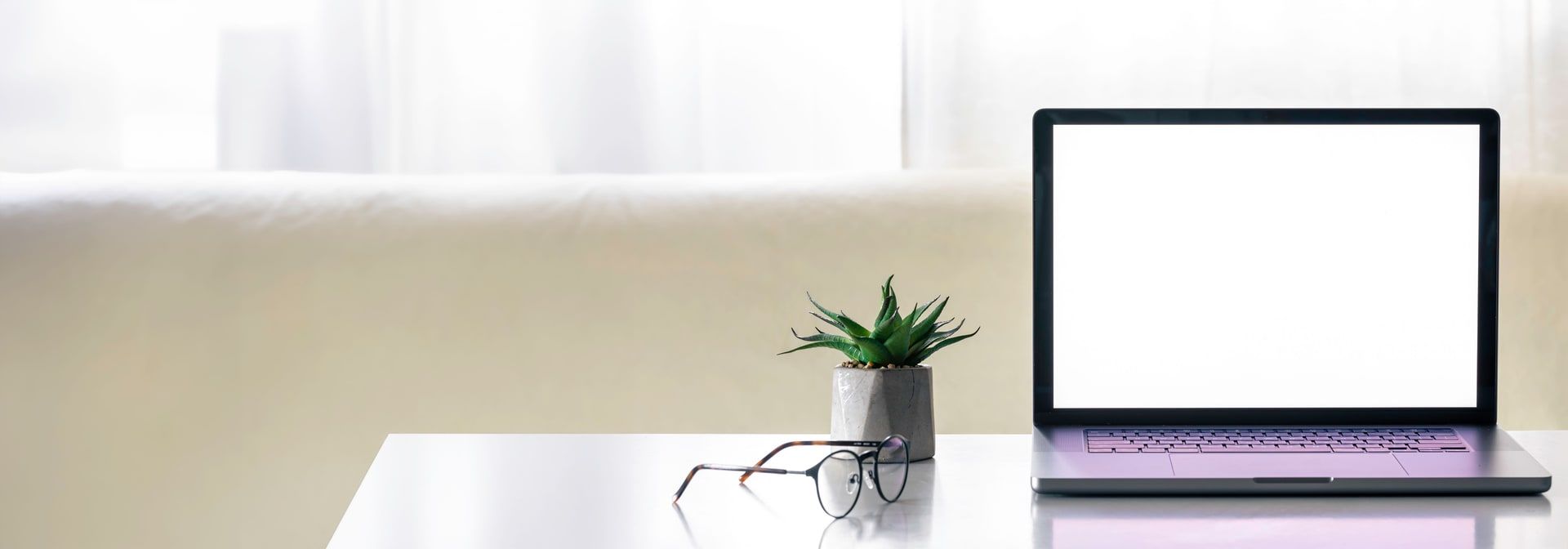 Ordinateur portable à écran vide posé sur une table claire, avec des lunettes et une plante